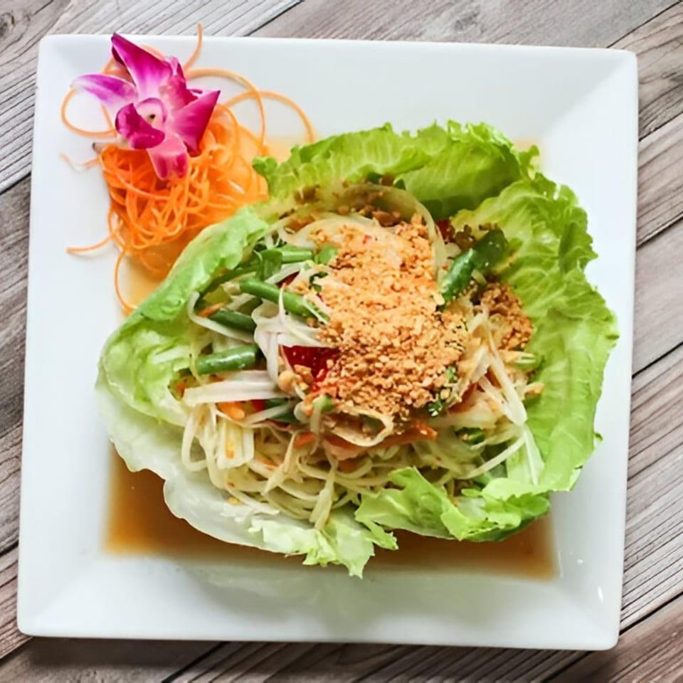 Som Tum, a Thai papaya salad with peanuts, green beans, and a purple orchid garnish.