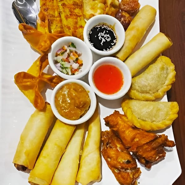 A large platter of assorted Thai appetizers including spring rolls, dumplings, and fried wontons with dipping sauces.