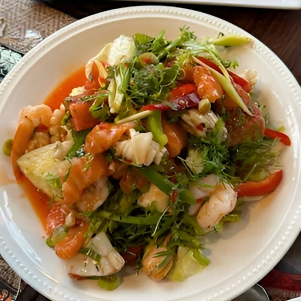 A vibrant Thai seafood salad with shrimp, squid, salmon, and fresh greens on a white plate.