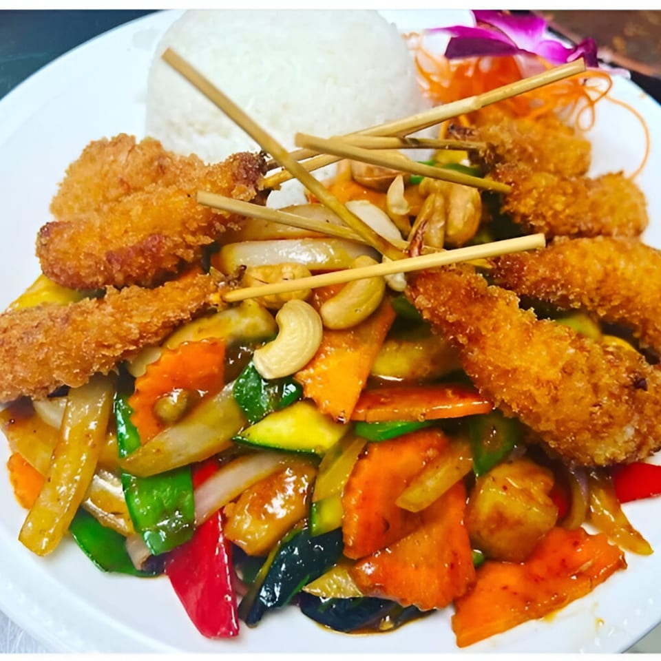 Crispy fried shrimp skewers with stir-fried vegetables, cashews, and white rice on a plate.