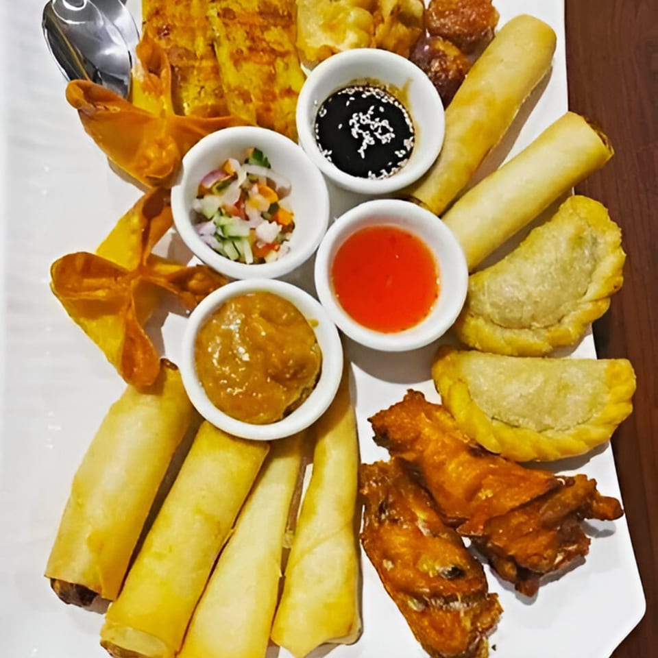 A large platter of assorted Thai appetizers, including spring rolls, dumplings, and dipping sauces.
