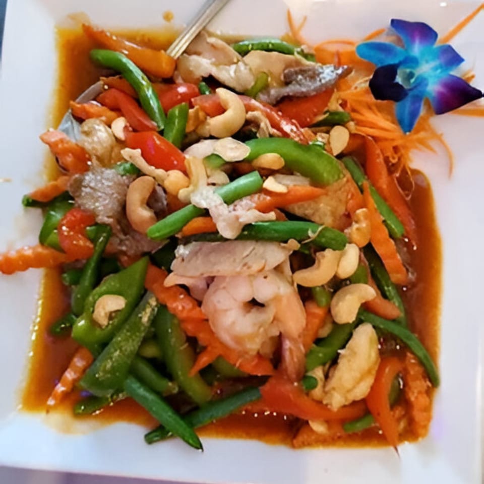 Thai stir-fry with shrimp, chicken, green beans, bell peppers, cashews, and a blue orchid garnish.
