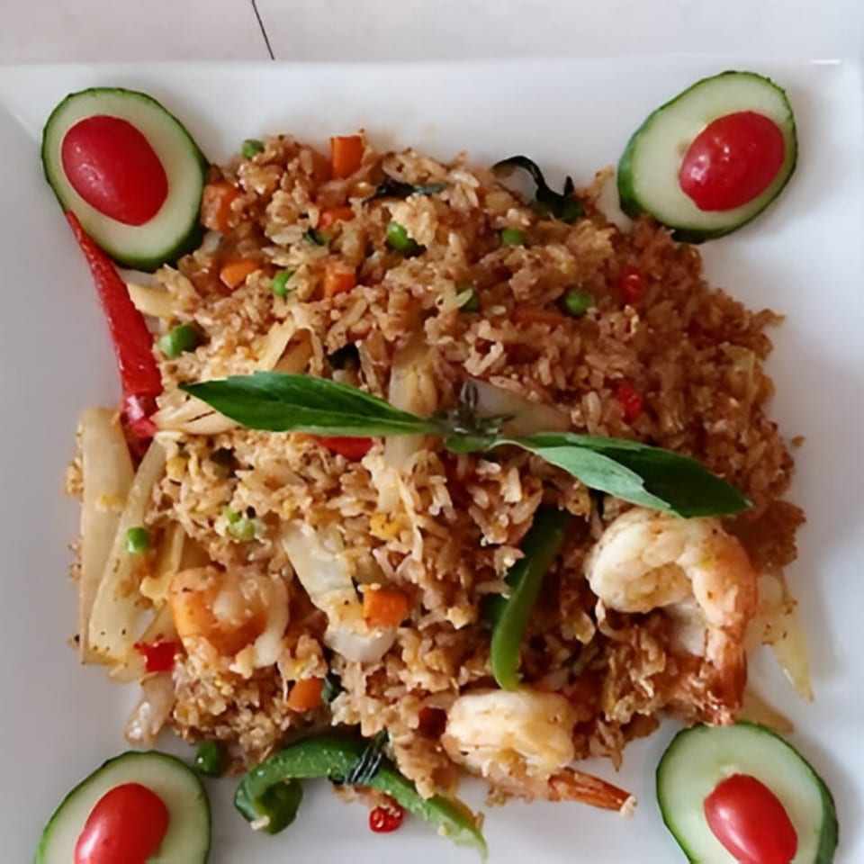 Thai fried rice with shrimp, vegetables, and basil, garnished with cucumber and cherry tomatoes.