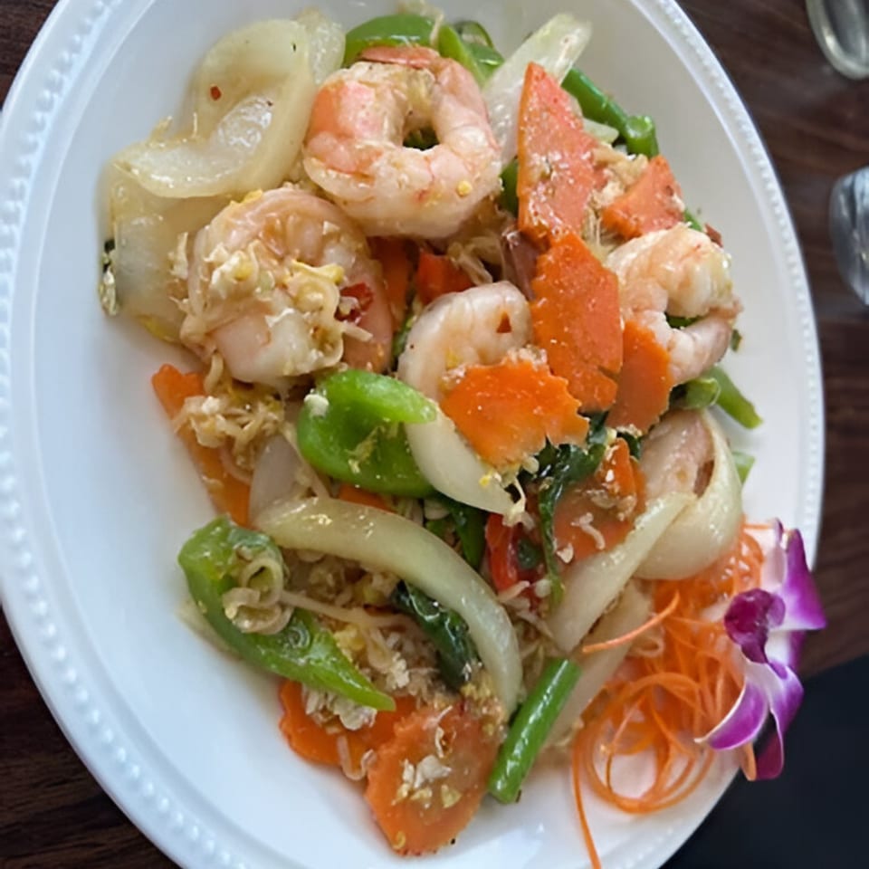 Thai stir-fried shrimp with carrots, bell peppers, and onions, garnished with an orchid.